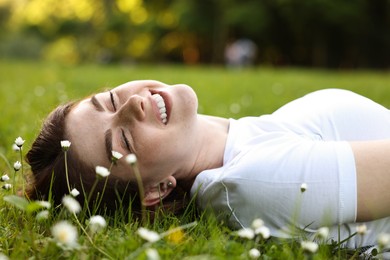 Portrait of smiling woman lying on grass and flowers. Spring vibes