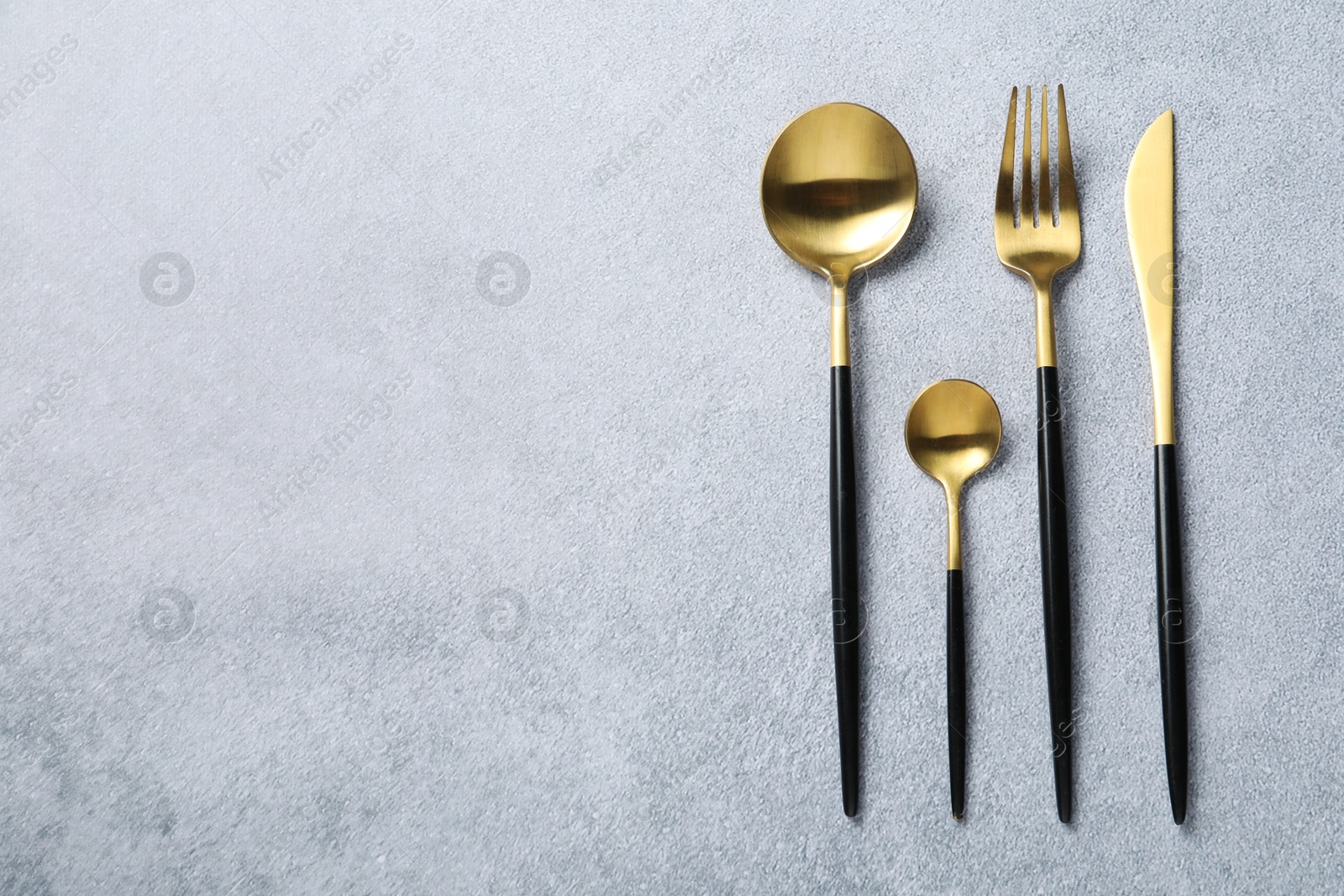 Photo of Stylish golden cutlery on grey table, flat lay. Space for text