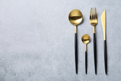 Photo of Stylish golden cutlery on grey table, flat lay. Space for text