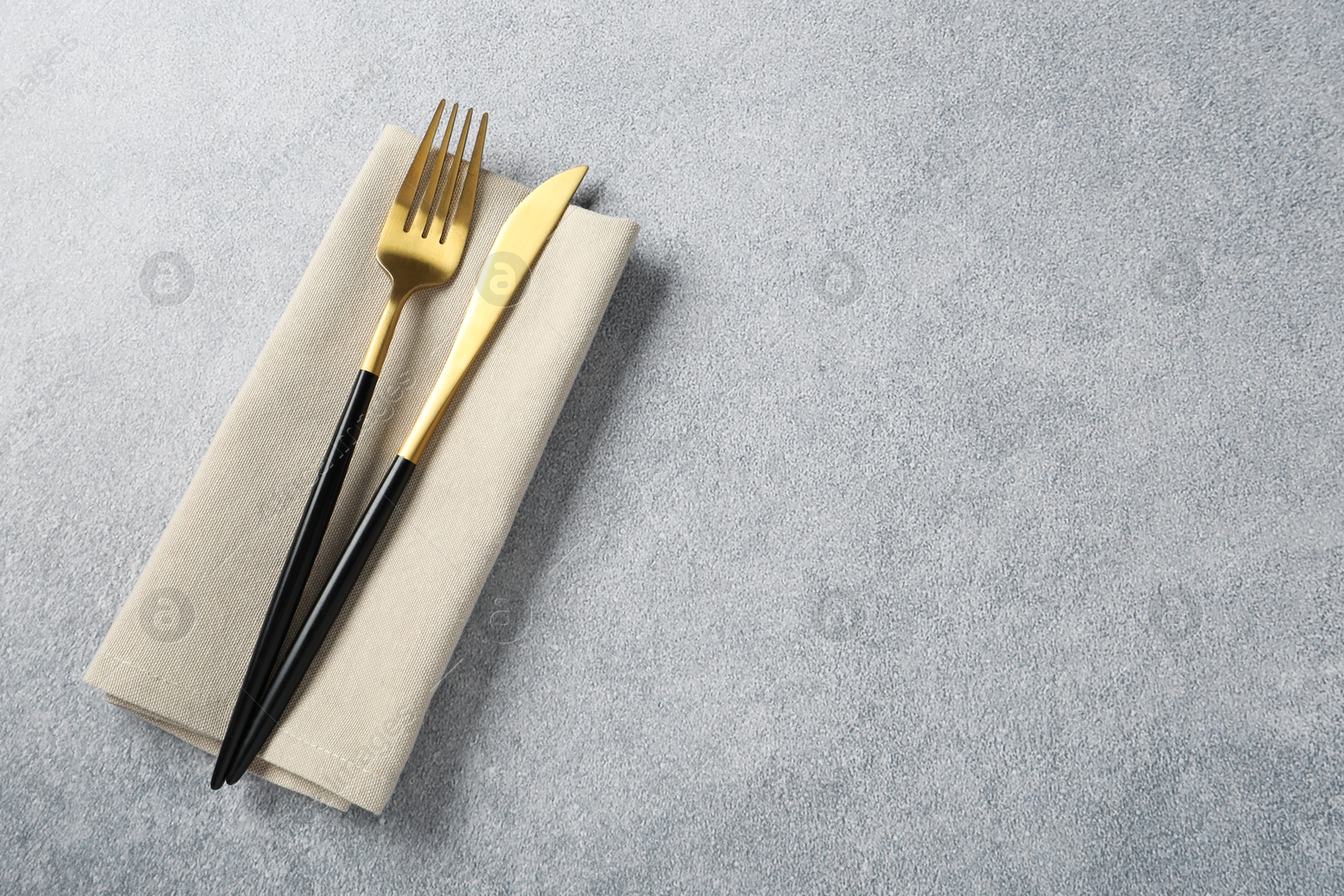 Photo of Stylish golden cutlery and napkin on grey table, top view. Space for text