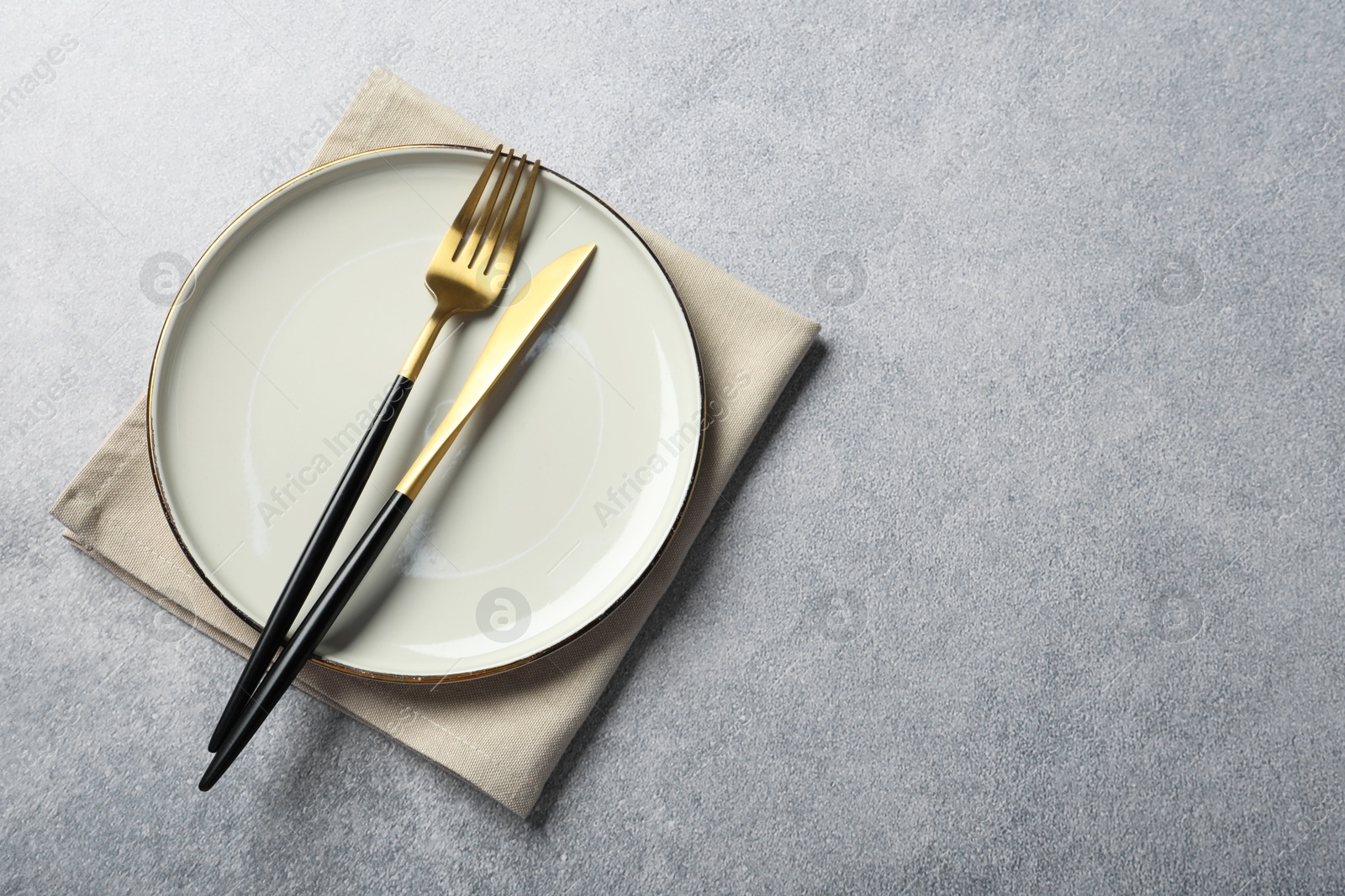 Photo of Stylish golden cutlery, plate and napkin on grey table, top view. Space for text