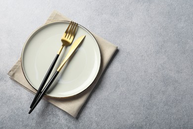 Stylish golden cutlery, plate and napkin on grey table, top view. Space for text