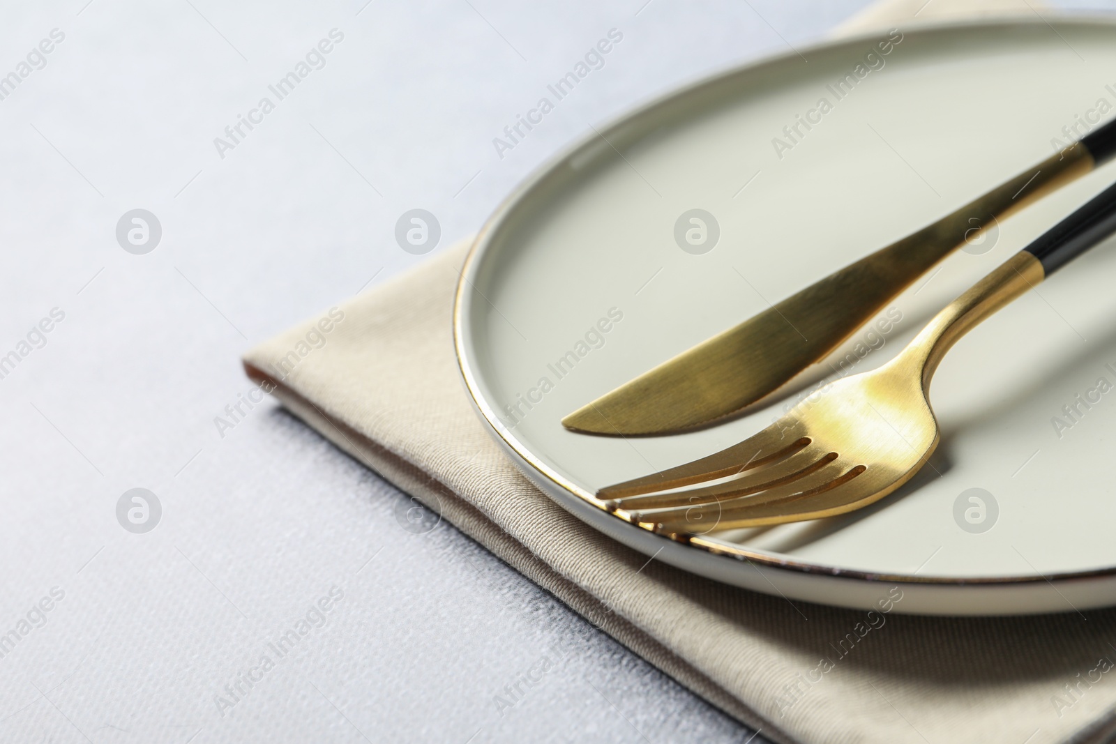 Photo of Stylish golden cutlery, plate and napkin on grey table, closeup. Space for text