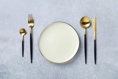 Stylish golden cutlery and plate on grey table, flat lay