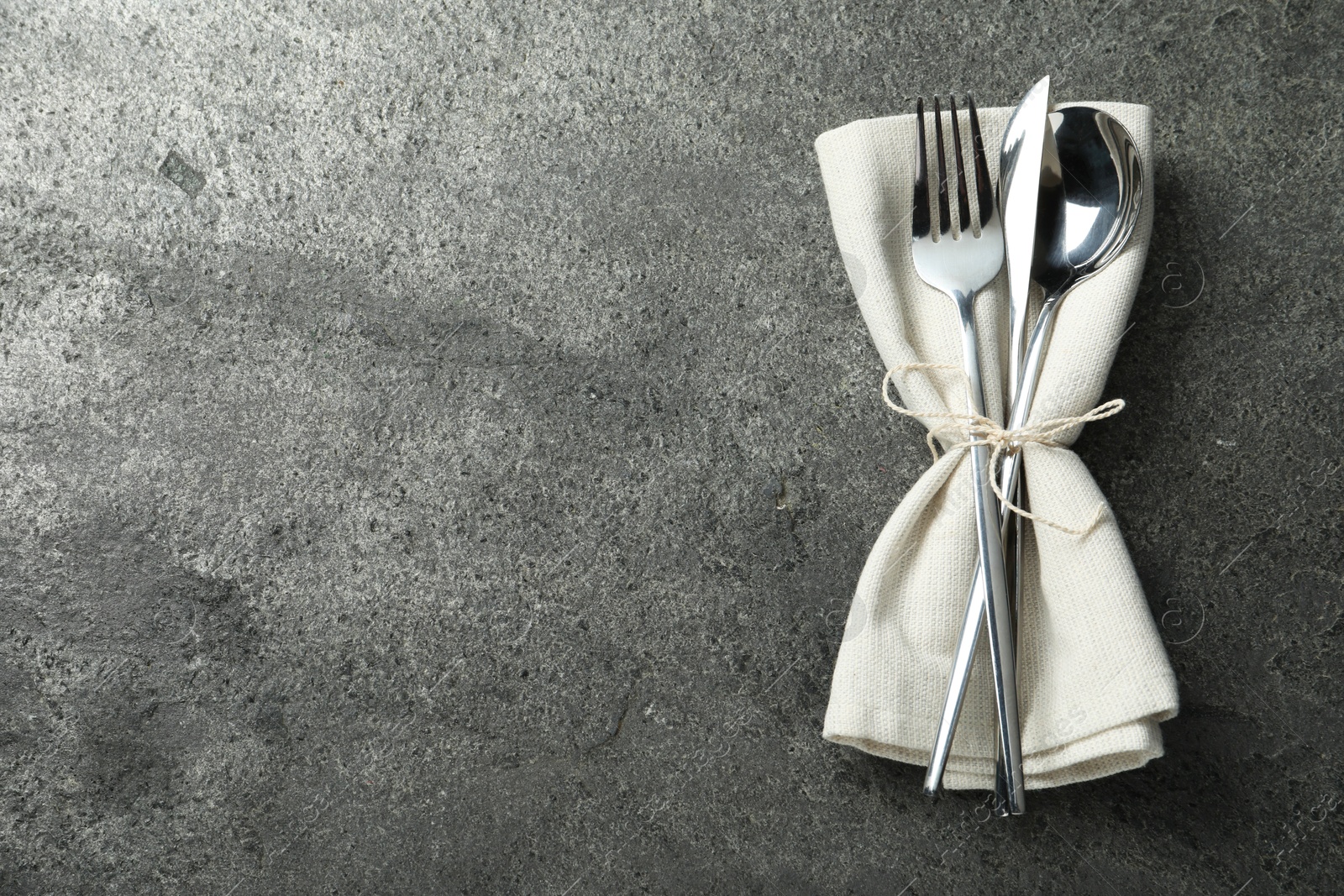 Photo of Stylish silver cutlery and napkin on grey table, top view. Space for text