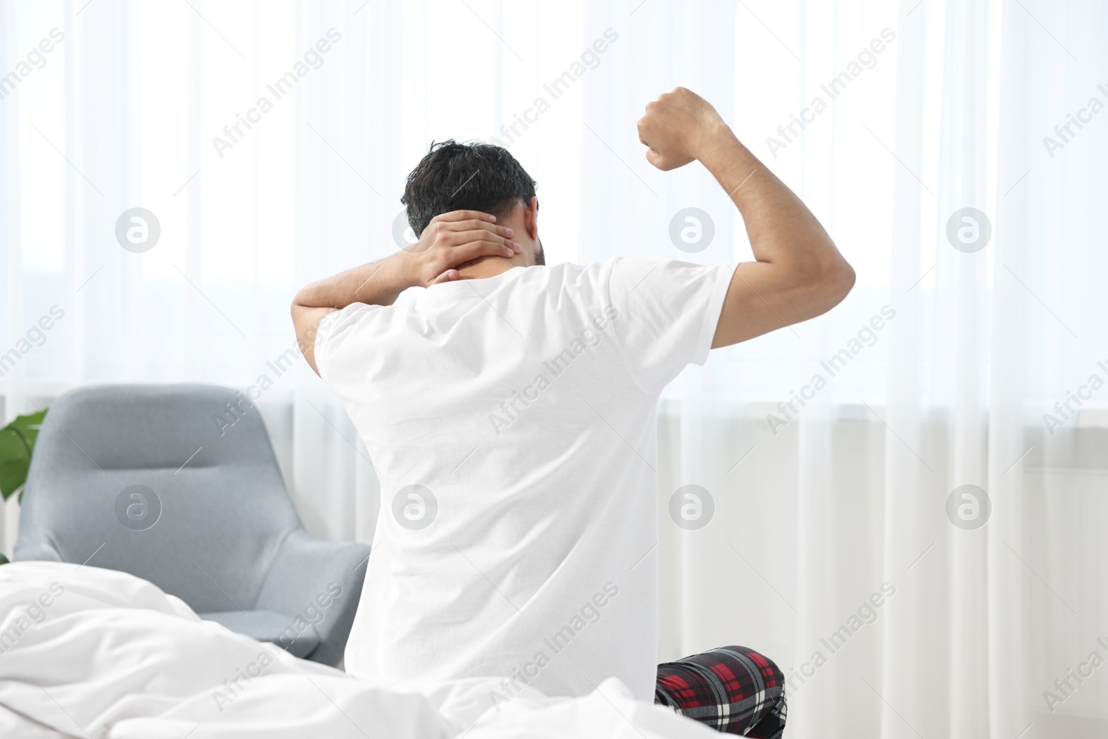 Photo of Morning of man stretching on bed at home, back view