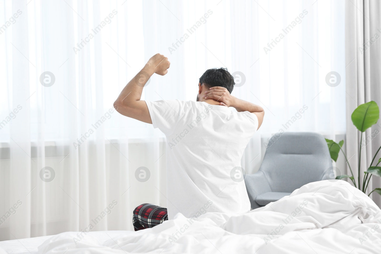 Photo of Morning of man stretching on bed at home, back view