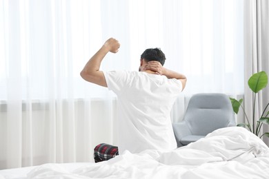 Morning of man stretching on bed at home, back view