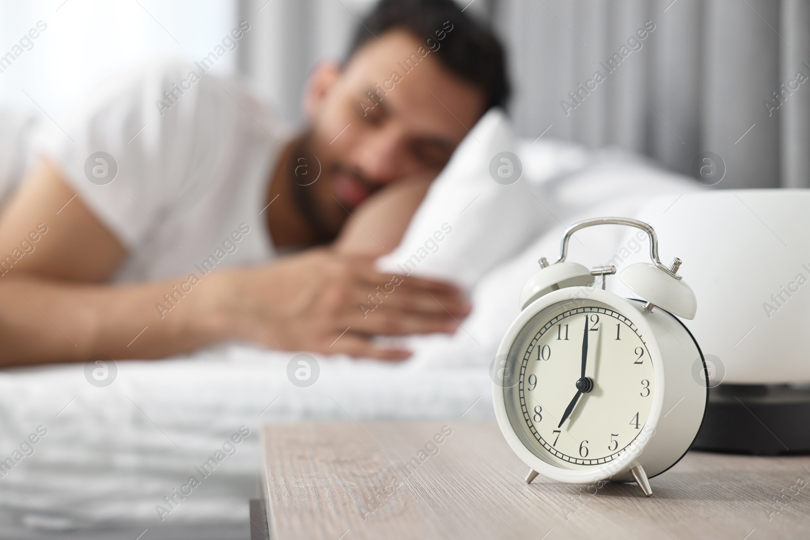 Photo of Man sleeping on bed at morning, focus on alarm clock