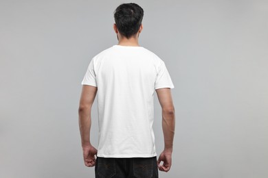 Man in white t-shirt on grey background, back view