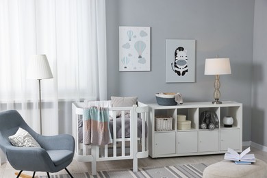 Newborn baby room interior with stylish furniture, comfortable crib and pictures of on wall