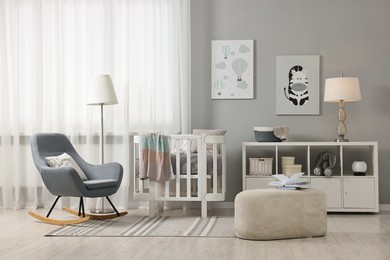 Newborn baby room interior with stylish furniture, comfortable crib and pictures of on wall