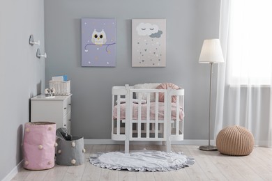 Newborn baby room interior with stylish furniture, comfortable crib and pictures of on wall