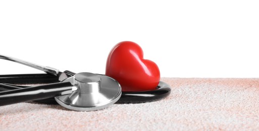 Photo of Stethoscope and red heart on color textured table against white background, space for text