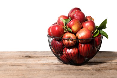 Photo of Fresh apples with green leaves in metal basket on wooden table against white background. Space for text