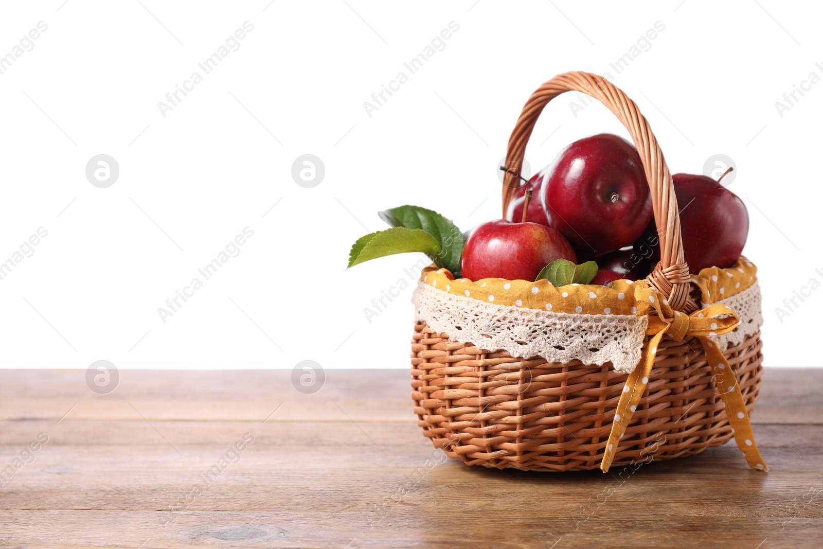 Photo of Fresh ripe red apples in wicker basket on wooden table against white background. Space for text