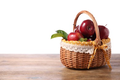 Photo of Fresh ripe red apples in wicker basket on wooden table against white background. Space for text