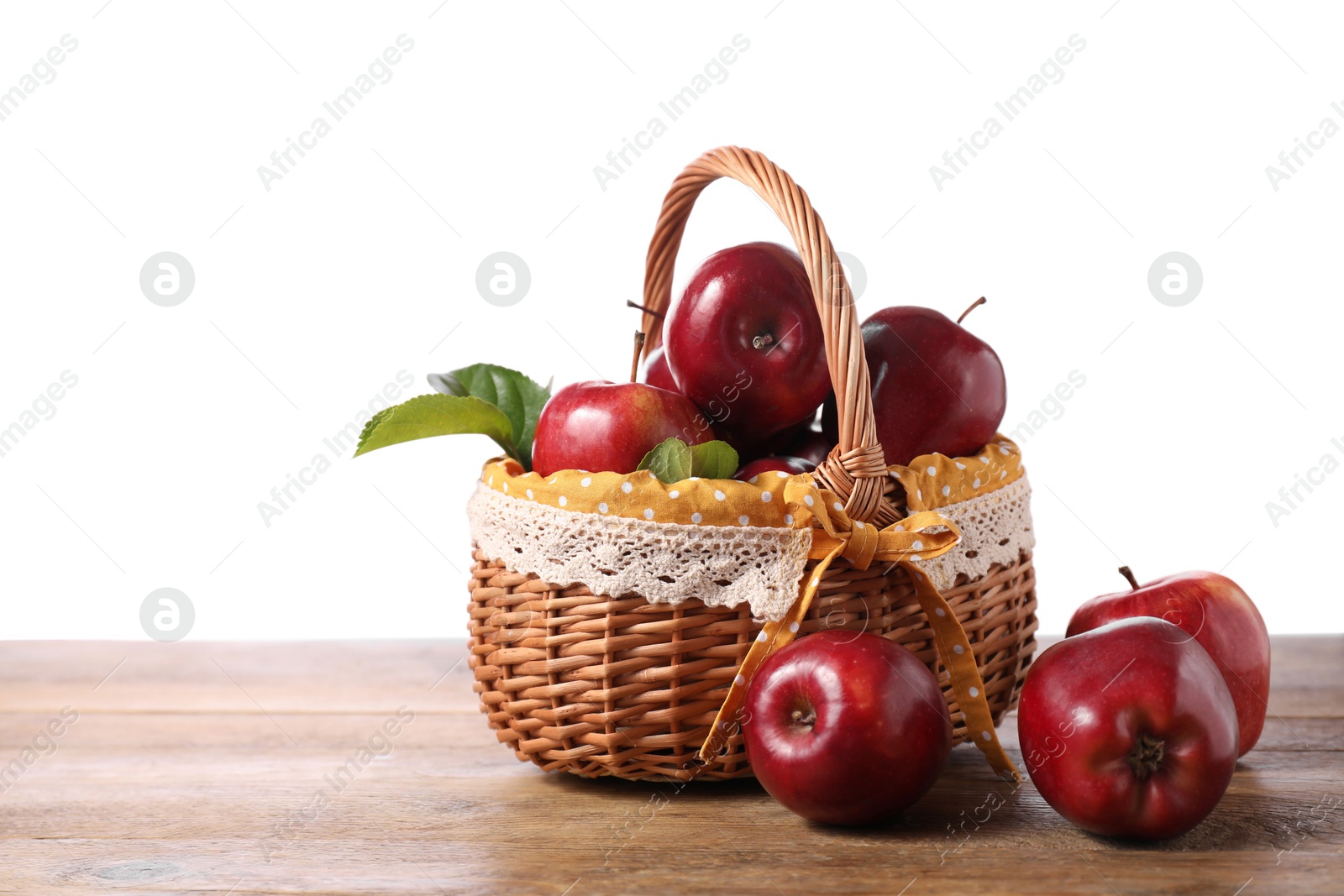 Photo of Fresh ripe red apples in wicker basket on wooden table against white background