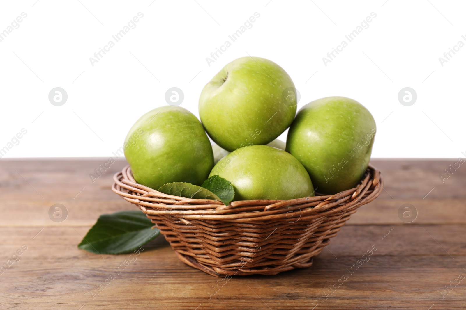 Photo of Ripe green apples in wicker basket on wooden table against white background