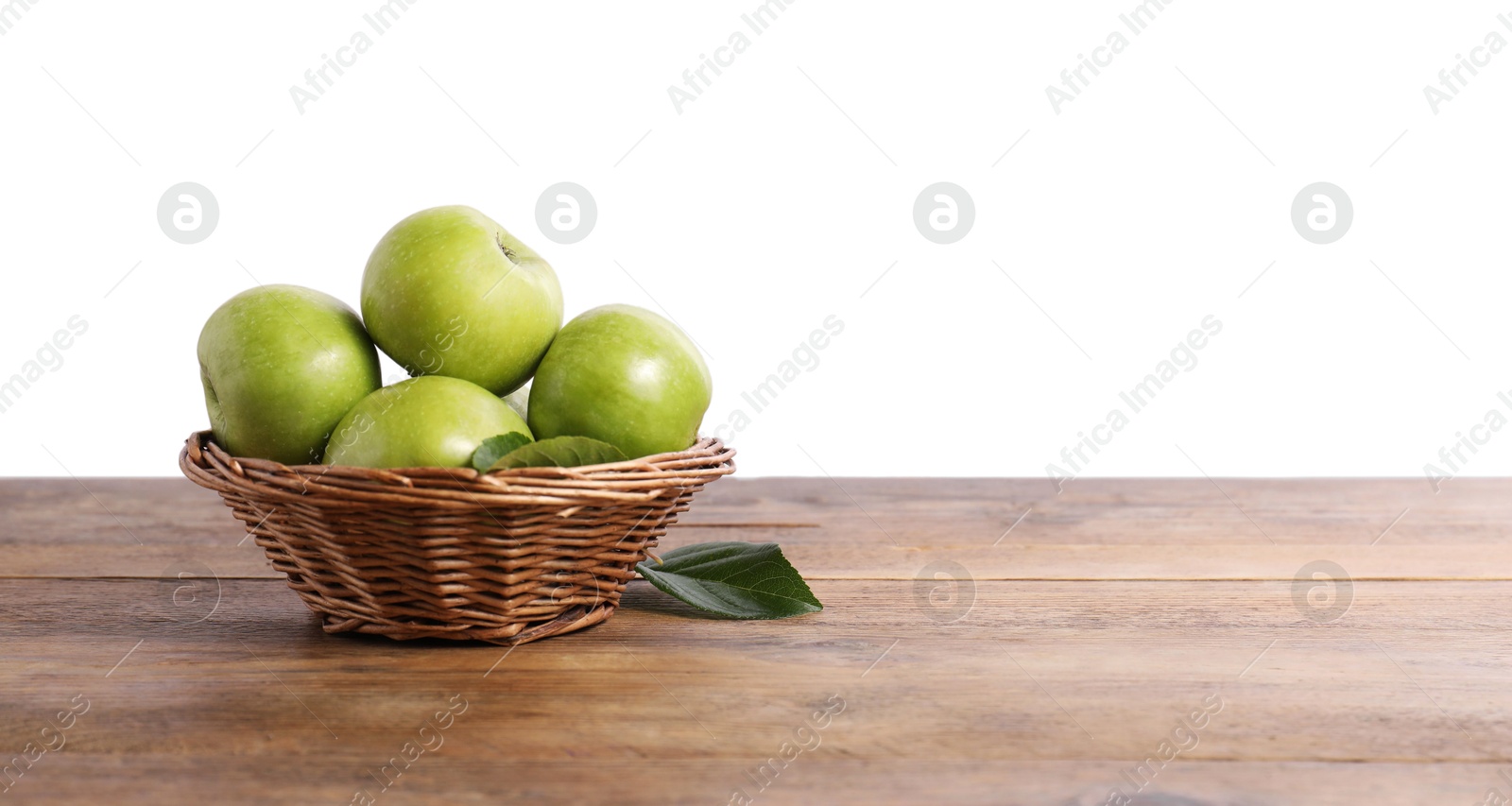 Photo of Ripe green apples in wicker basket on wooden table against white background. Space for text