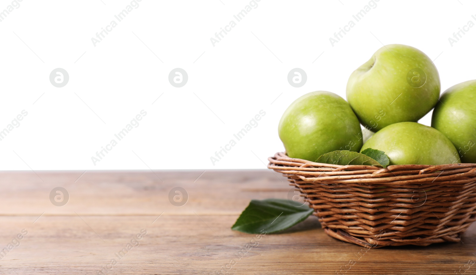 Photo of Ripe green apples in wicker basket on wooden table against white background. Space for text