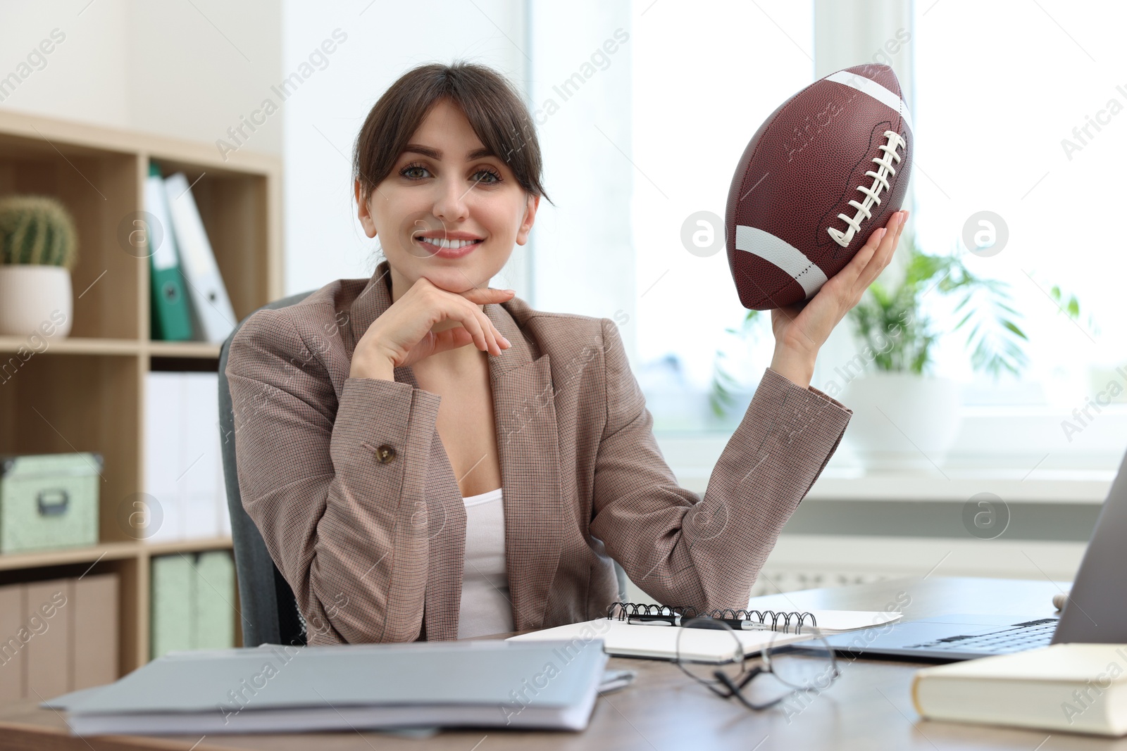 Photo of Smiling employee with american football ball at table in office