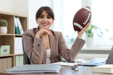 Smiling employee with american football ball at table in office