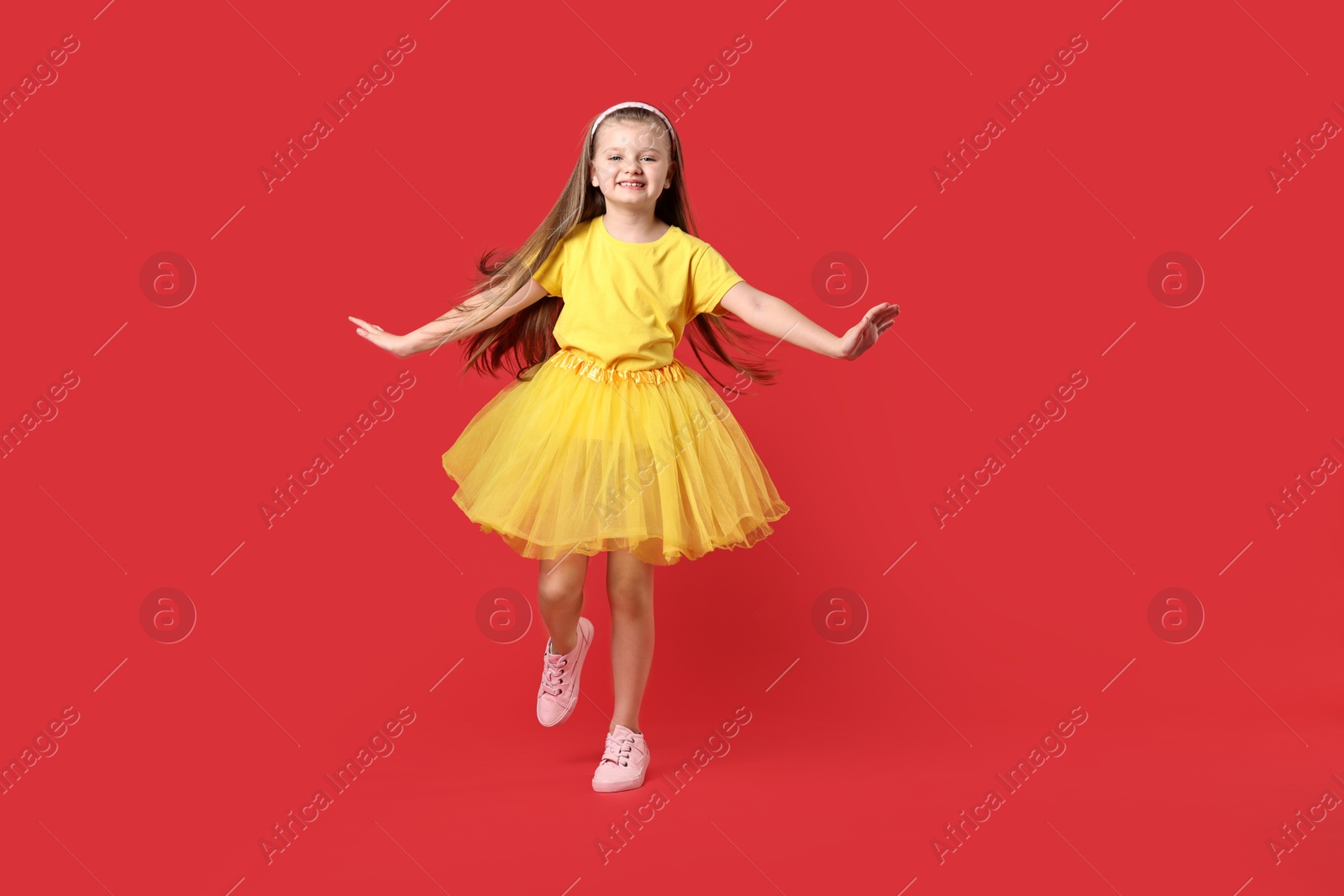 Photo of Cute little girl dancing on red background, space for text