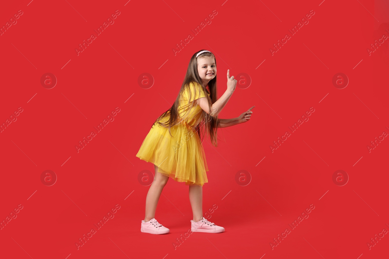 Photo of Cute little girl dancing on red background