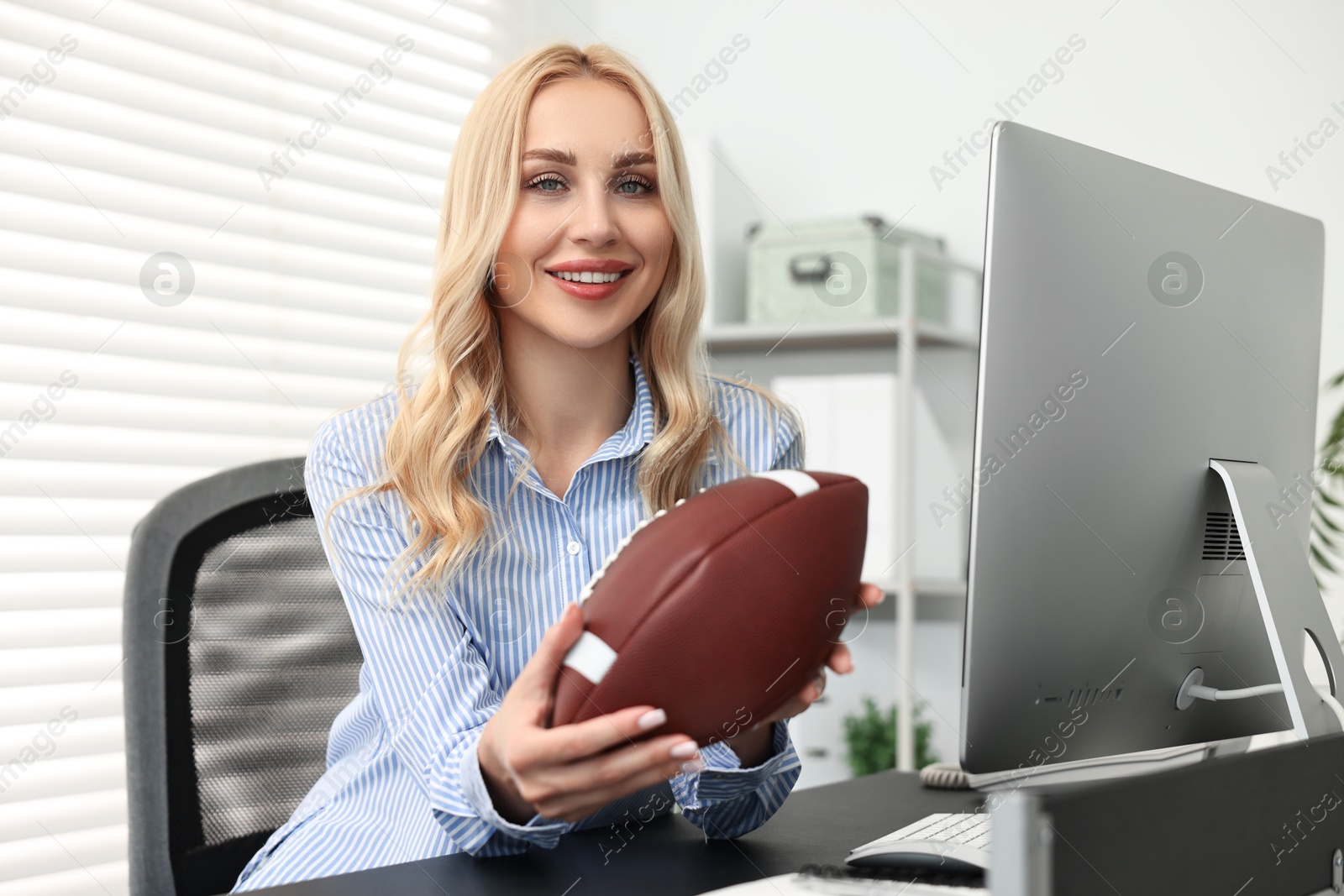 Photo of Happy woman with american football ball at table in office