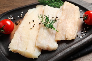 Raw cod fish, dill, tomatoes and spices on wooden table, closeup