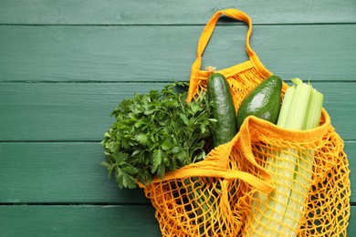 Photo of String bag with different vegetables on green wooden table, top view. Space for text