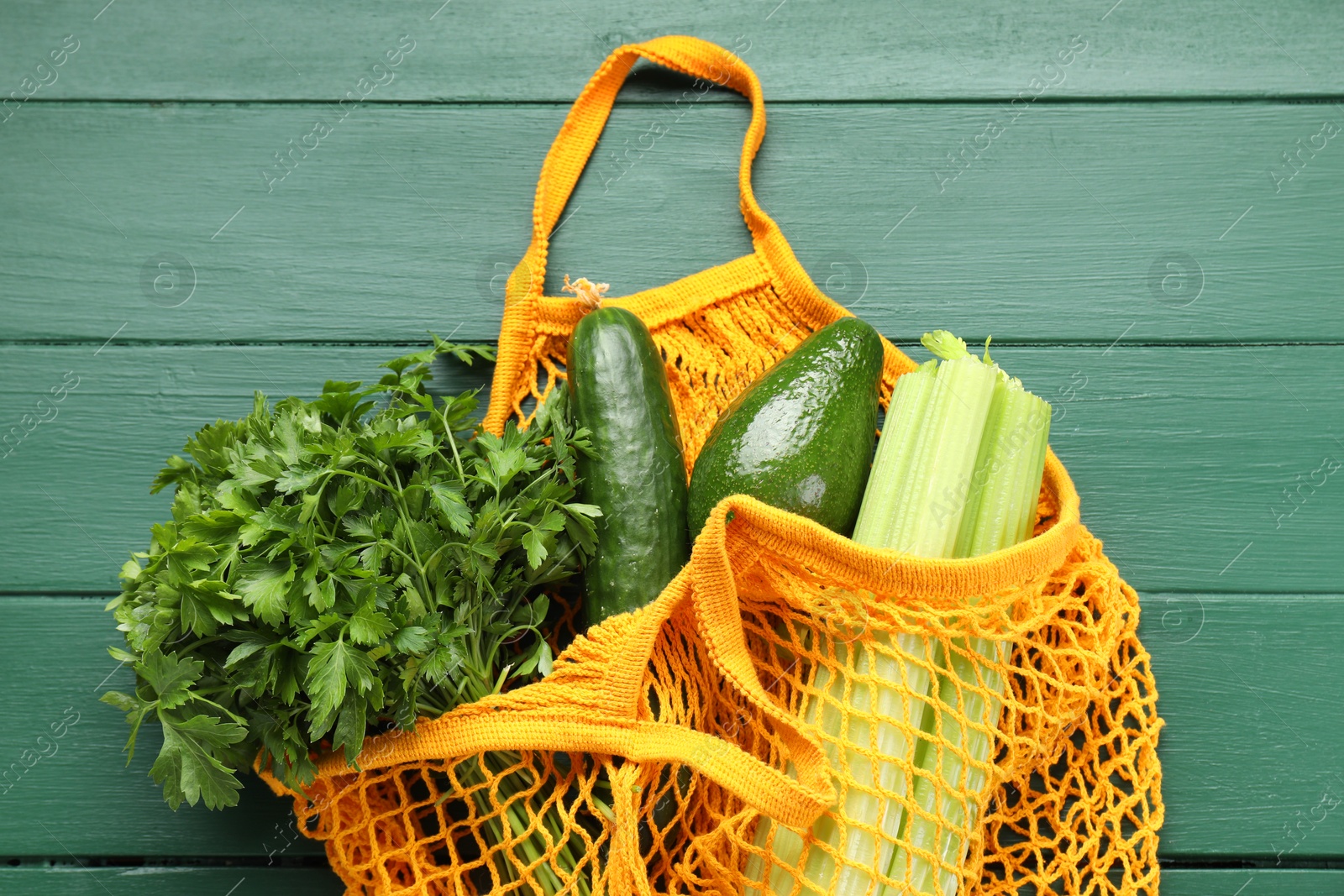 Photo of String bag with different vegetables on green wooden table, top view