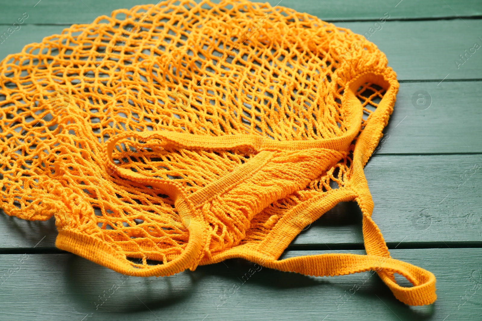 Photo of Orange string bag on green wooden table, closeup