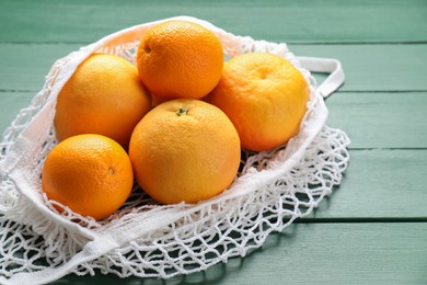 Photo of String bag with oranges on green wooden table, closeup