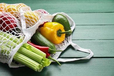 Photo of String bag with different vegetables on green wooden table, closeup. Space for text