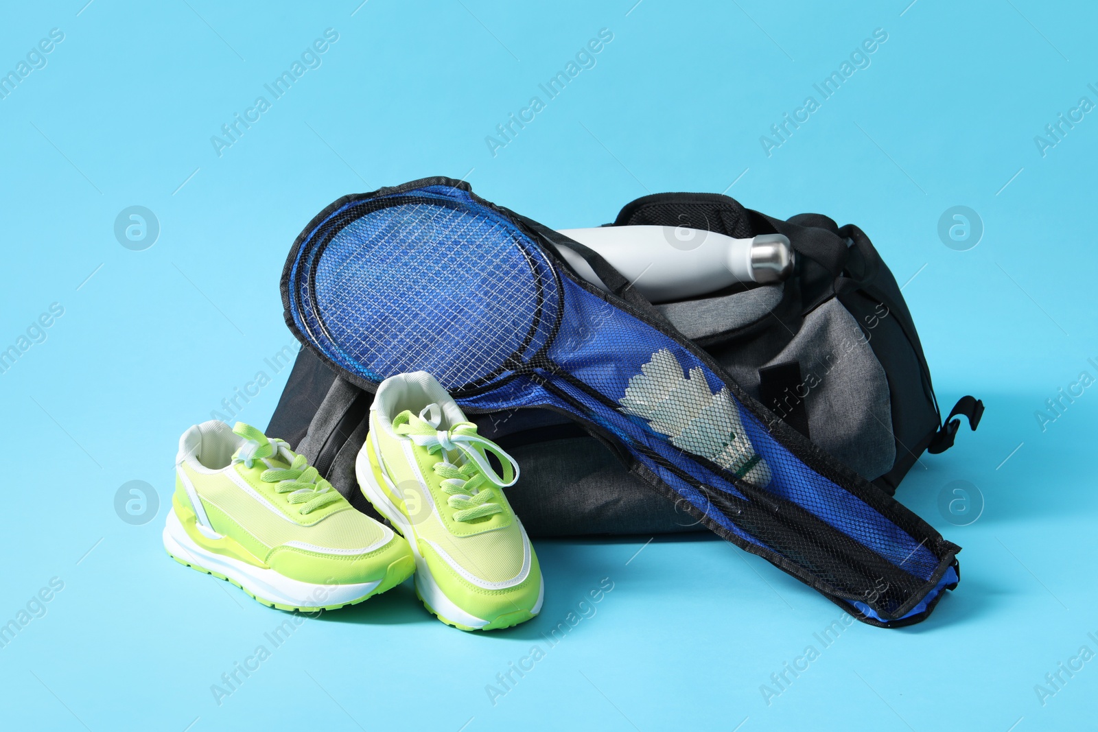 Photo of Badminton set, bag, sneakers and bottle on light blue background