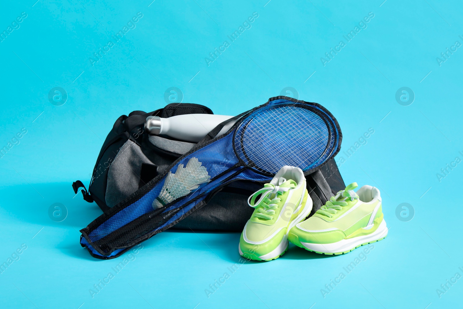 Photo of Badminton set, bag, sneakers and bottle on light blue background