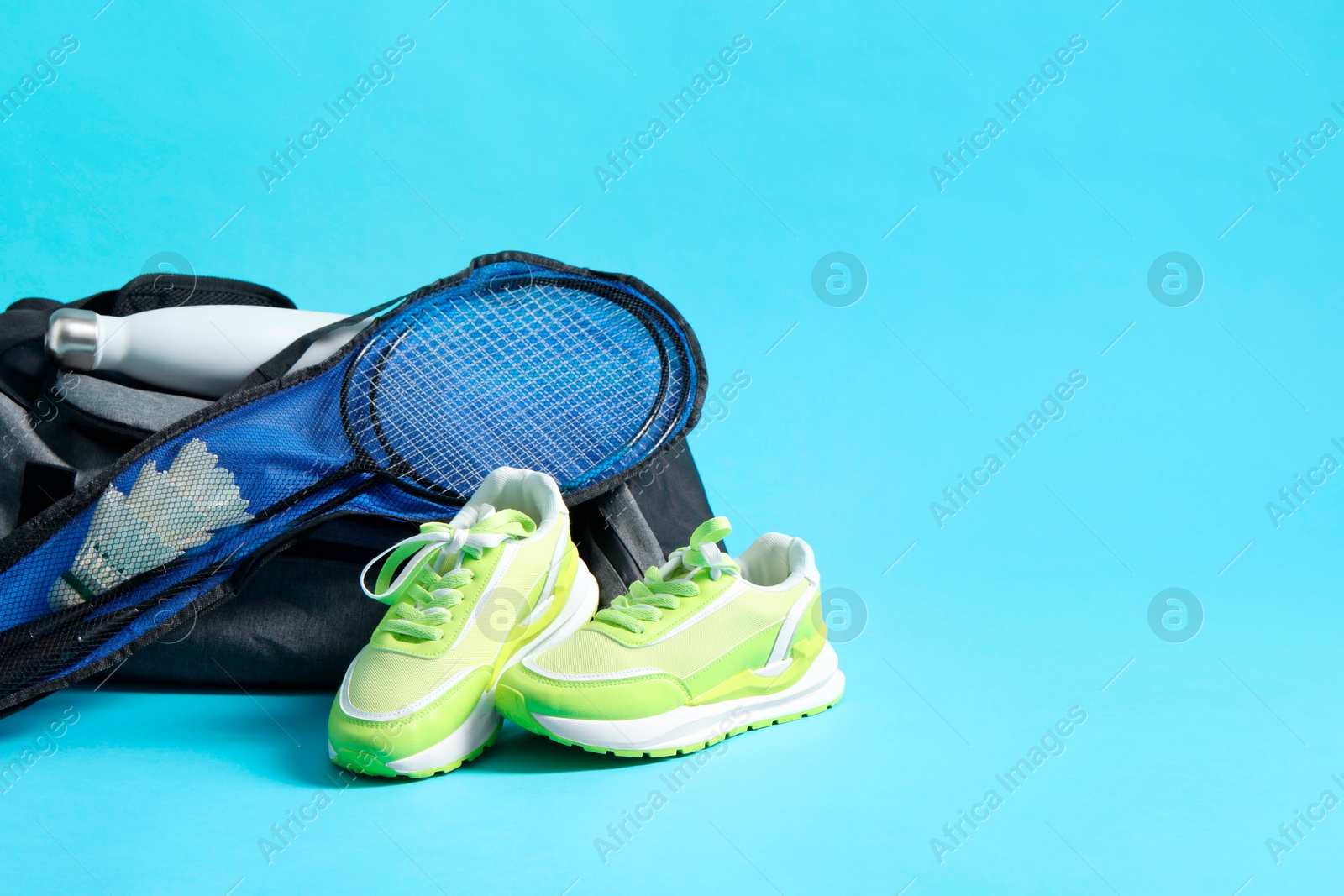Photo of Badminton set, bag, sneakers and bottle on light blue background, space for text