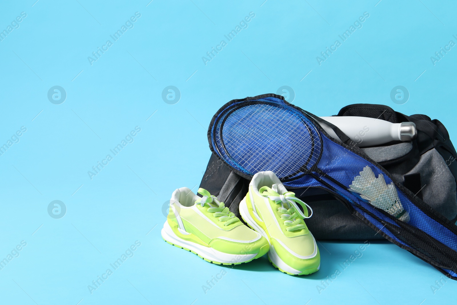 Photo of Badminton set, bag, sneakers and bottle on light blue background, space for text