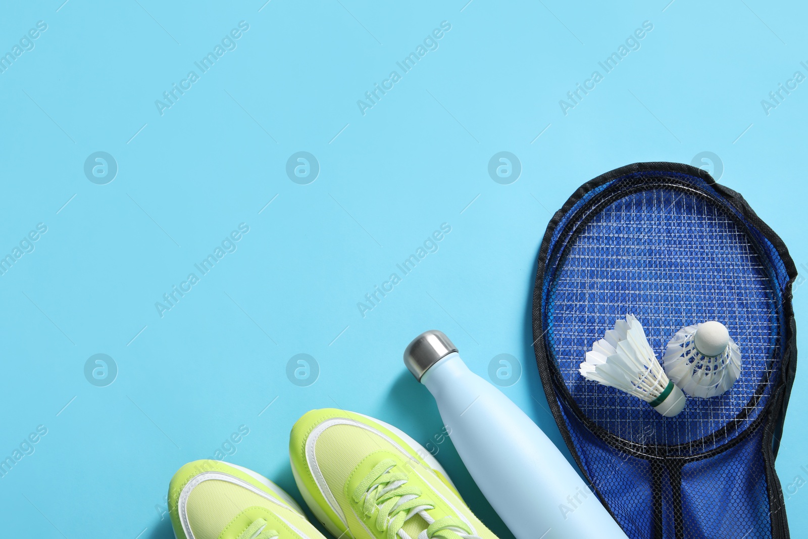 Photo of Badminton set, sneakers and bottle on light blue background, flat lay. Space for text