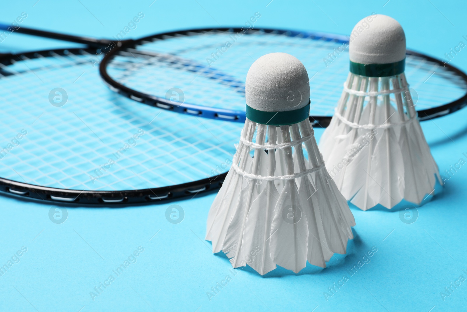 Photo of Feather badminton shuttlecocks and rackets on light blue background, closeup