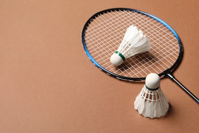 Feather badminton shuttlecocks and racket on brown background, space for text