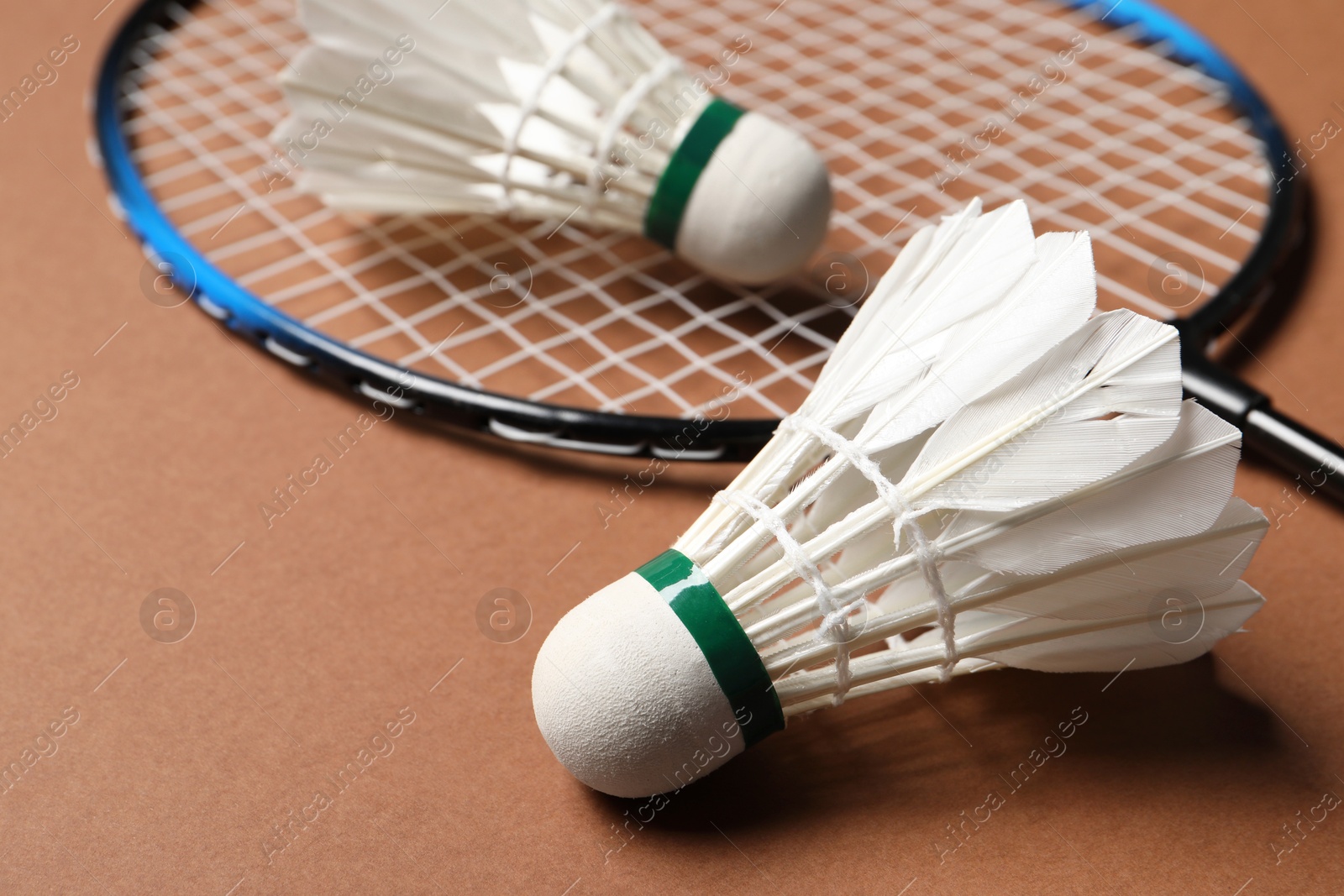 Photo of Feather badminton shuttlecocks and racket on brown background, closeup