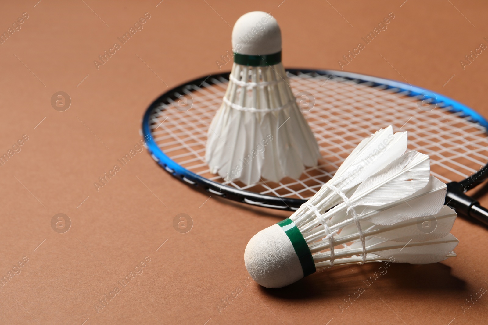 Photo of Feather badminton shuttlecocks and racket on brown background, closeup