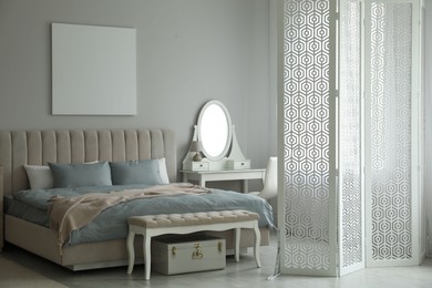 Folding screen, mirror and comfortable bed in bedroom. Interior design