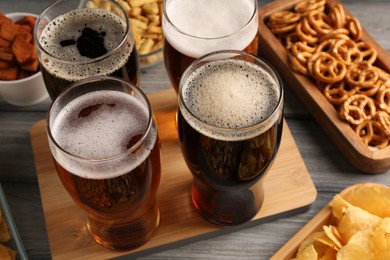 Glasses with different types of beer and snacks on grey wooden table