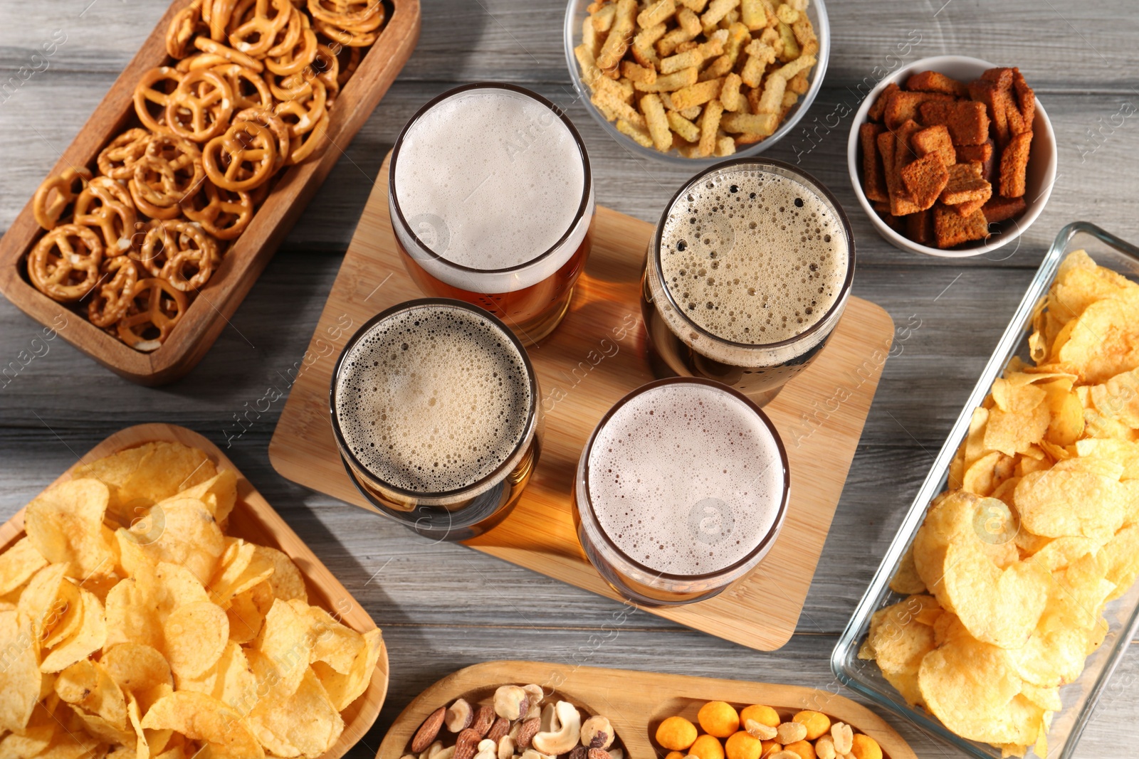 Photo of Glasses with different types of beer and snacks on grey wooden table, flat lay