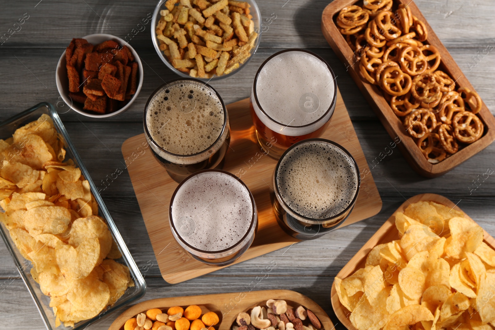 Photo of Glasses with different types of beer and snacks on grey wooden table, flat lay