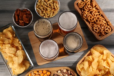 Glasses with different types of beer and snacks on grey wooden table, flat lay